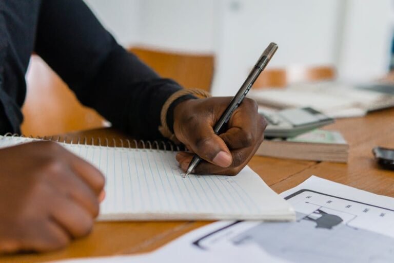 Close-up of hand writing on notebook at a wooden table, featuring paper and ballpen.