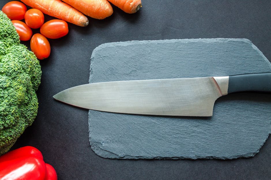 Close-up of fresh vegetables with a chef's knife on a rustic slate board.