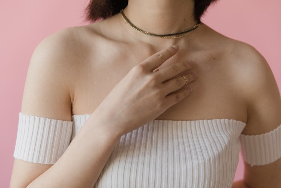 Close-up of a woman in a white off-shoulder top and necklace against a pink background.