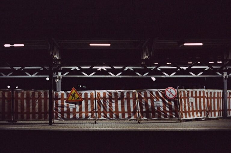 Railway station platform at night with construction signs and fenced barriers, highlighting urban development.