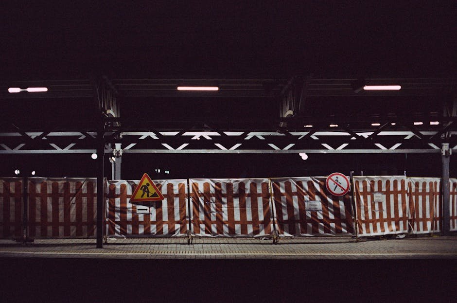 Railway station platform at night with construction signs and fenced barriers, highlighting urban development.